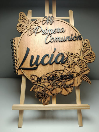 Álbum de comunión de madera con detalles 3D de mariposas y flores. Incluye el nombre 'Lucía' y la fecha 10-05-2020. Izmi Láser Regalos Personalizados.